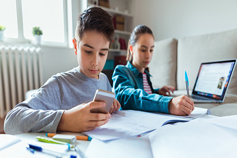 A boy and a girl using a cell phone and a computer to enhance their learning in the classroom.