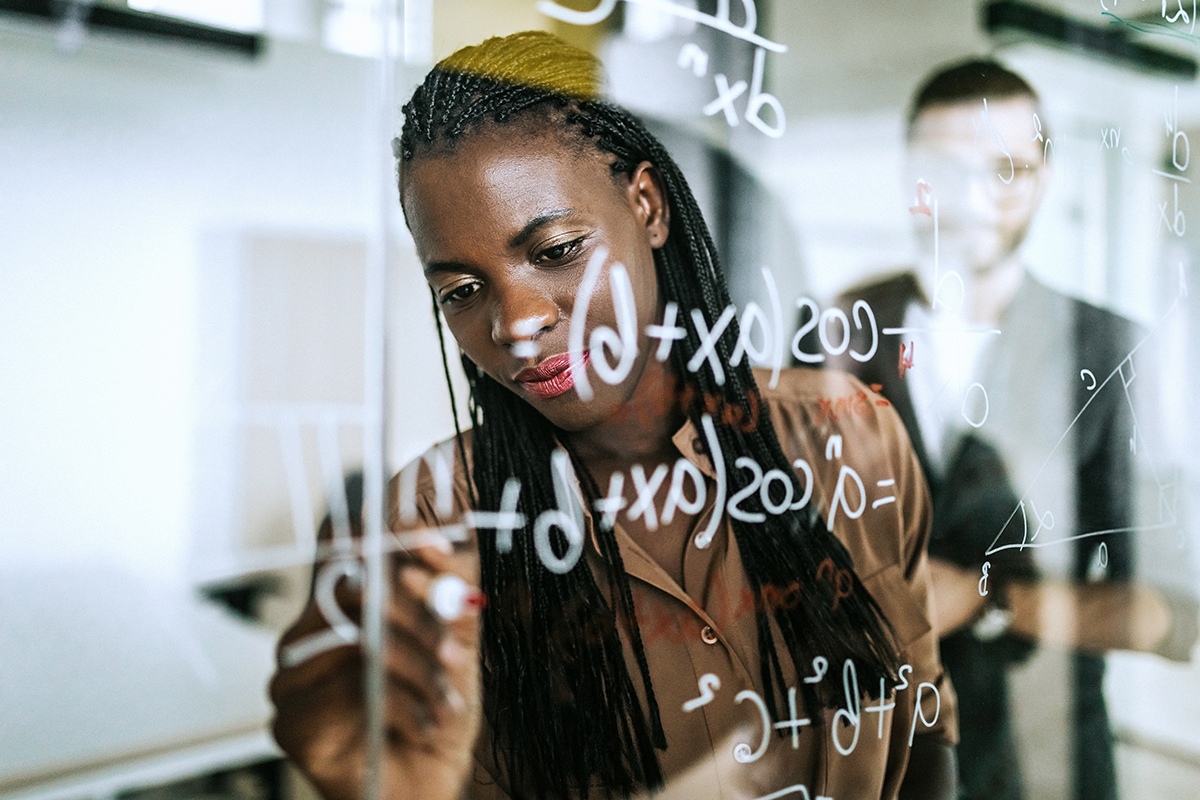 Colleagues Writing Mathematical Formulas On Transparent Wipe Board.