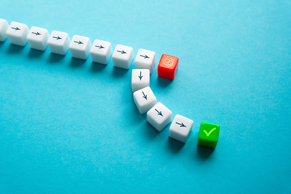 A row of white cubes with a black arrow simulates the path of a project, until it meets a red cube that represents the problems and forces the white cubes to take another path to reach the green cube. 