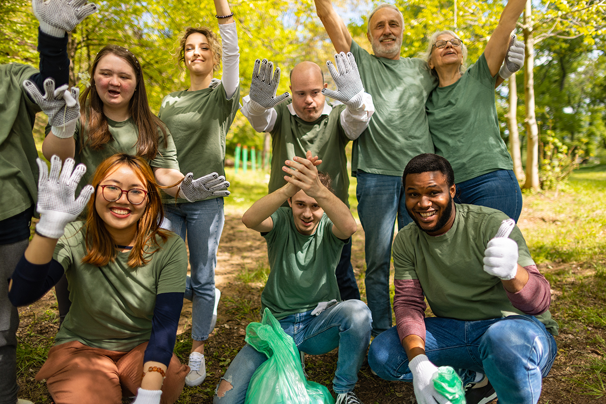 Multiracial group of volunteers waving to camera after collecting garbage in a forest