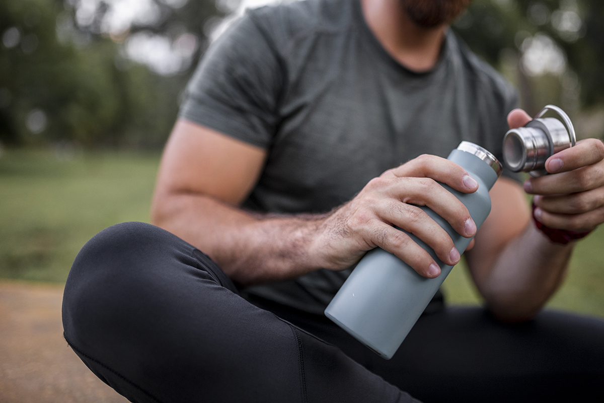 Close-up of a reusable water bottle in a human hand, concept of thirst, rehydration and decrease of single-use plastic.