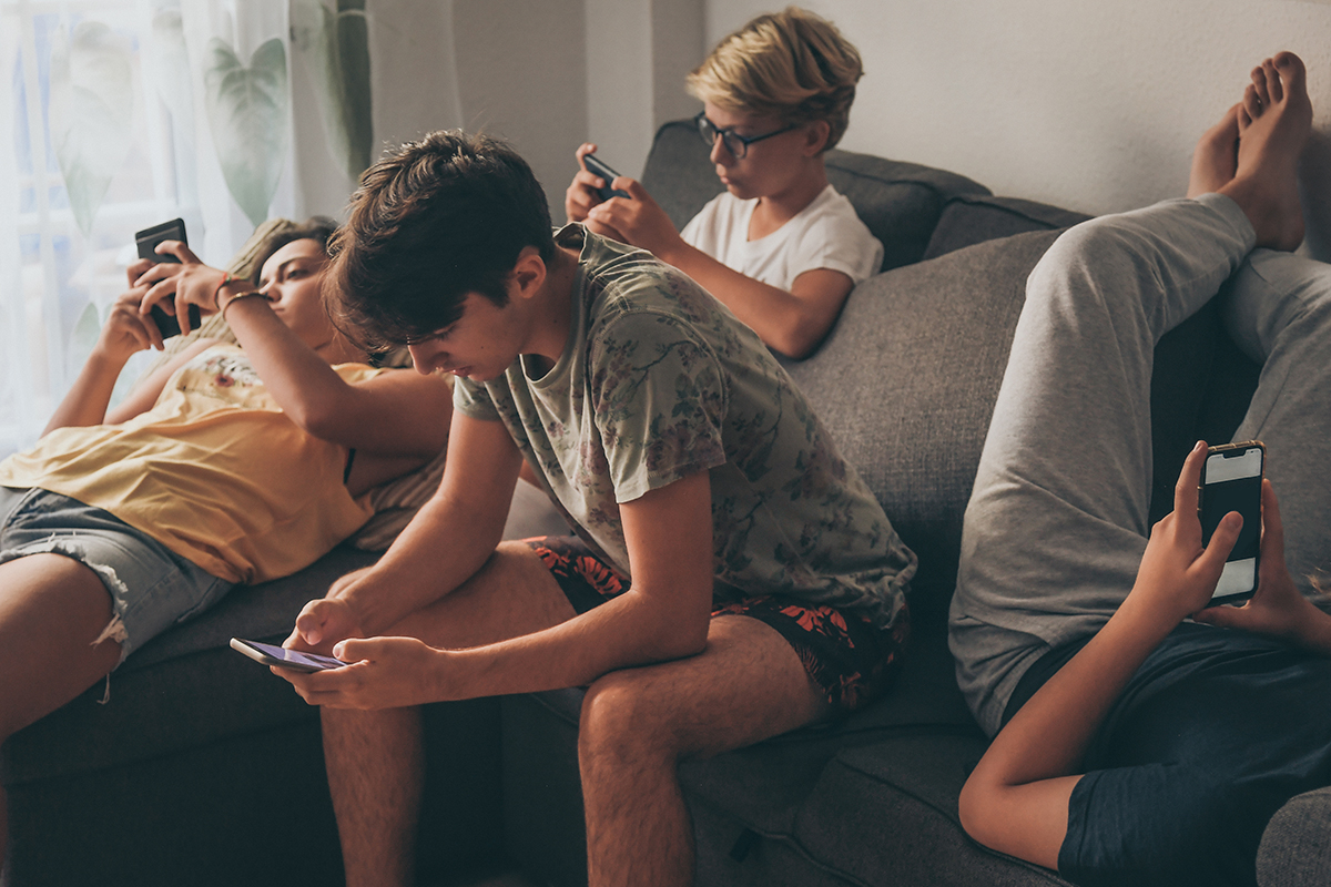 Group of teenagers using a smartphone sitting on the sofa at home. Young boys and a girl sharing photo and video watching an online social story. Friends enjoying new technological trends. Concept of youth and technology.