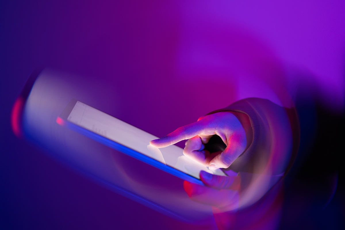 Hand interacting with a touch screen against a backdrop of neon lights.