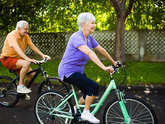 Two older adults engaging in physical exercise (riding bicycles) to improve their health.
