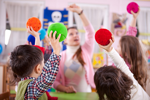 Um professor e crianças a brincar com bolas numa sala de aula, praticando educação e entretenimento. 
