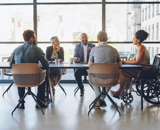 Mulher em cadeira de rodas em grupo falando sobre inclusão na empresa.