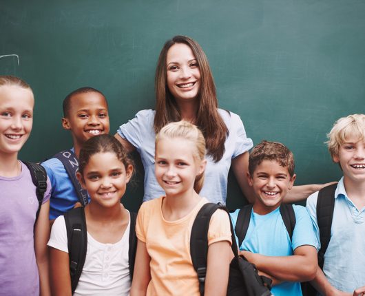 Un alegre grupo de escolares ante la pizarra con su guapa profesora.