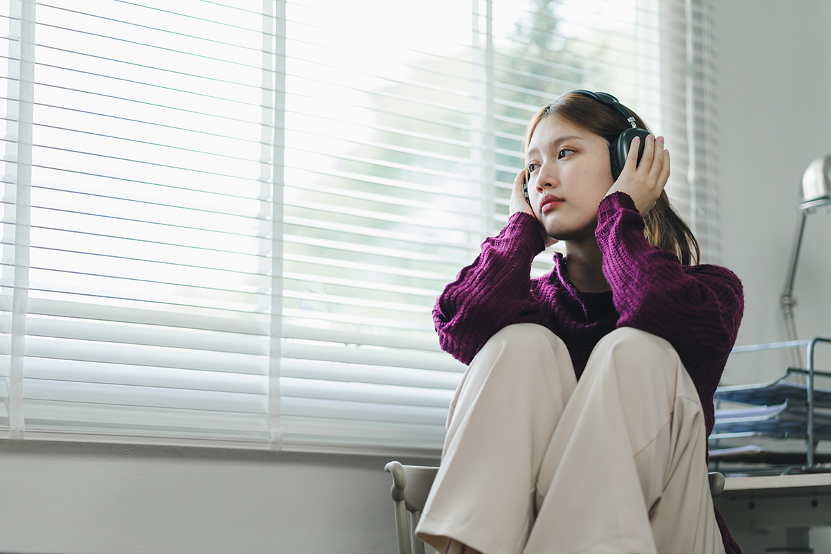 Menina ouve música com seus fones de ouvido enquanto olha pela janela.