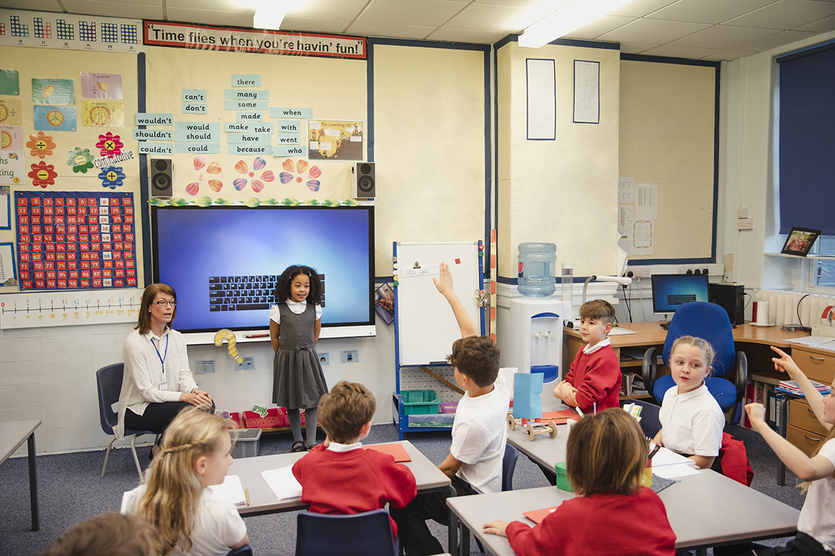 Uma aluna do ensino fundamental apresenta seu trabalho para a classe com o apoio da professora ao seu lado. Esta é uma escola em Hexham, Northumberland, no nordeste da Inglaterra.