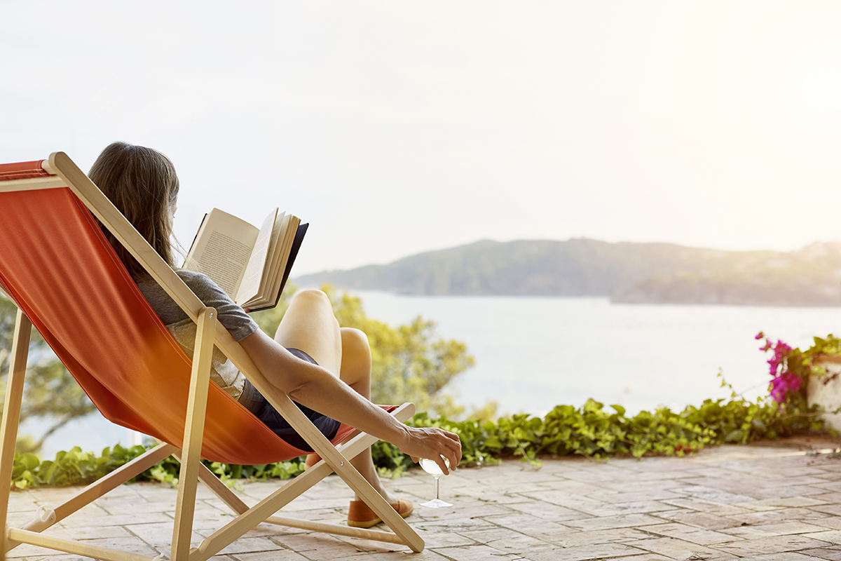 Benefícios do descanso. Mulher lendo um livro enquanto relaxa em uma espreguiçadeira no quintal.

