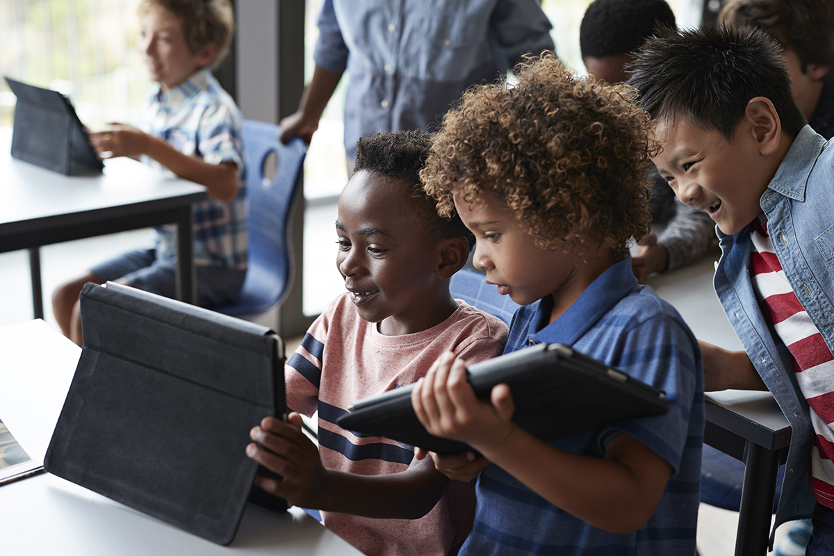 Três meninos usam seus tablets na sala de aula. 