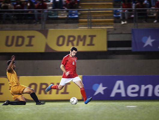 Jogadores de futebol num estádio com uma multidão ao fundo.