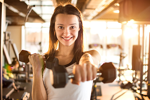 Una joven realizando pesas de mano en un gimnasio para el fortalecimiento muscular. 