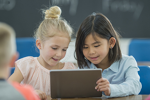 Dos niñas de diversas culturas éticas viendo una tablet en su escuela. 