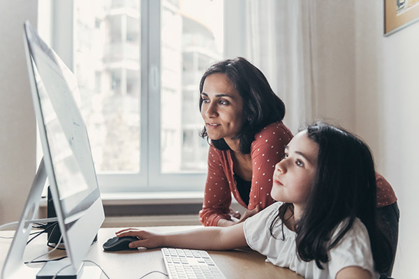 Una madre y su hija pequeña utilizan una computadora de escritorio. 
